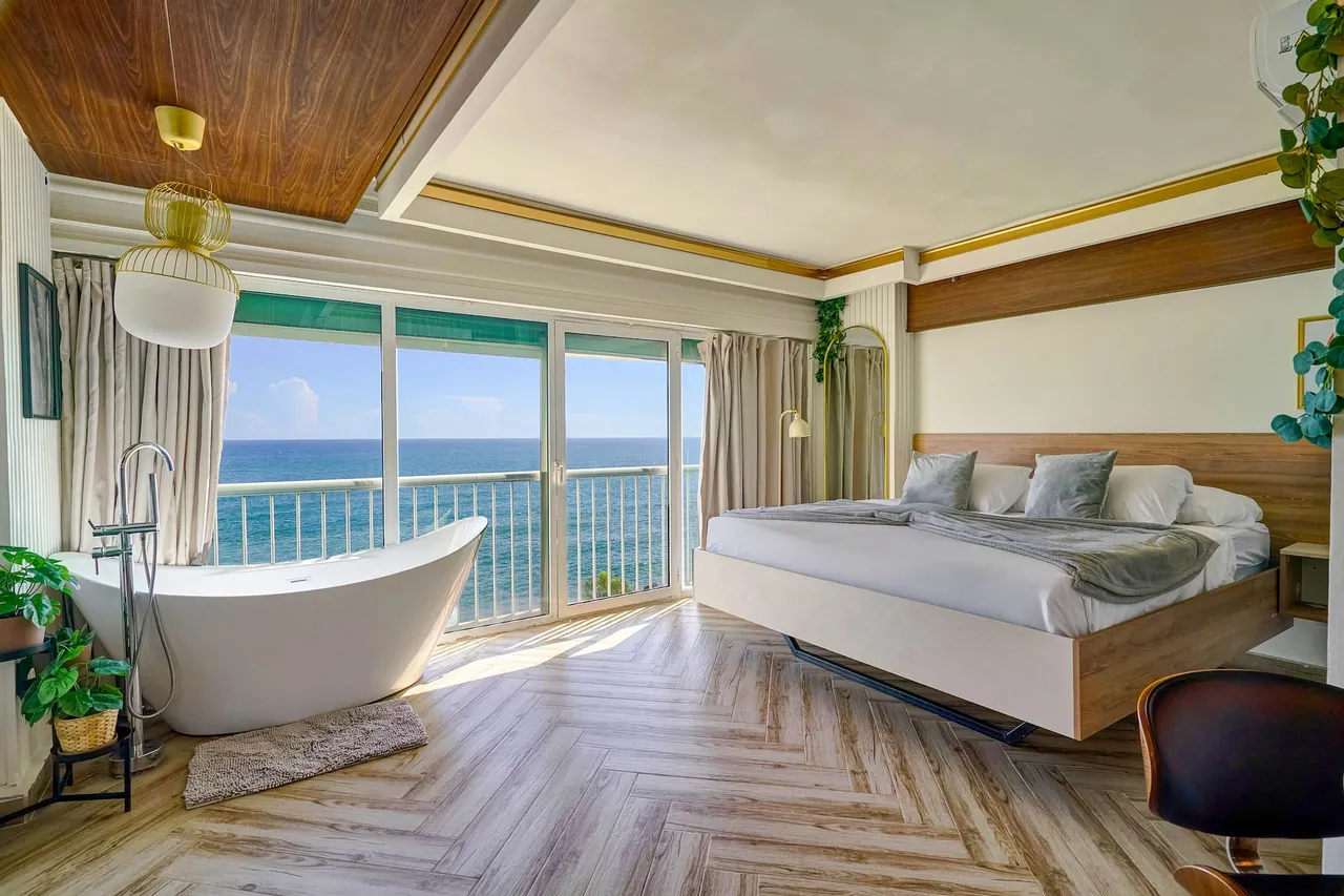 Studio with a slipper bathtub, king bed and wood-panel ceiling over the sea